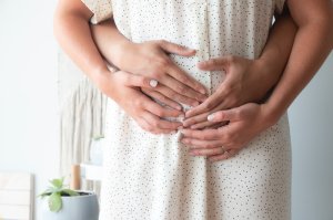 Pregnant woman with partner's hands around her stomach